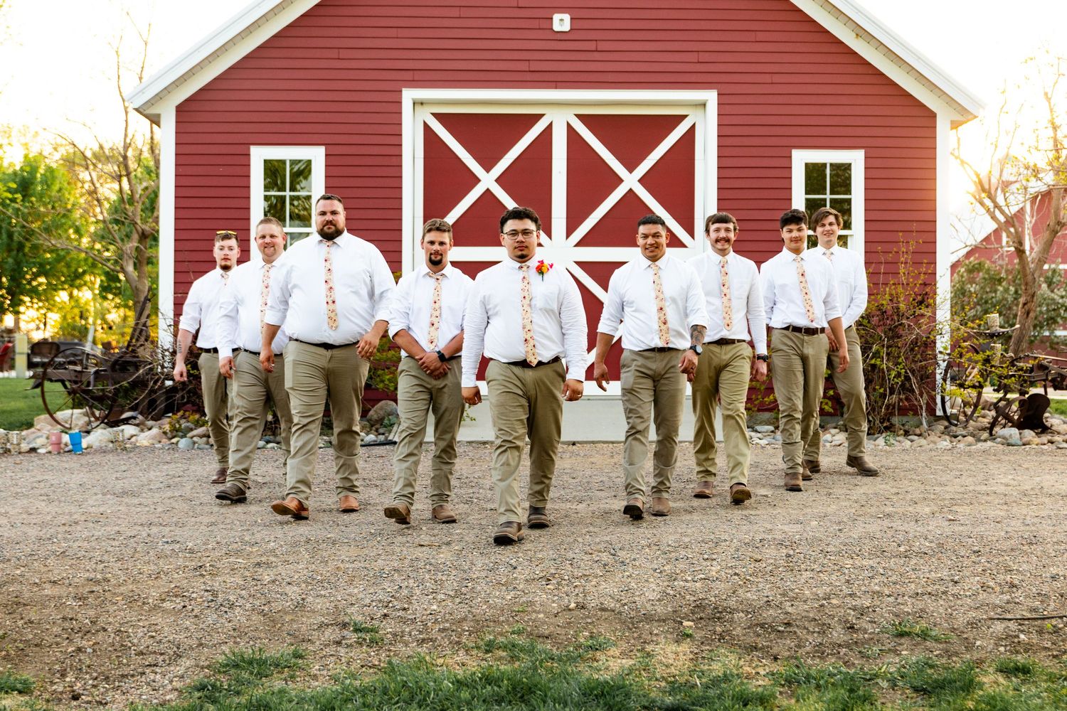 Wedding party members in casual attire posed along the front of a red barn.