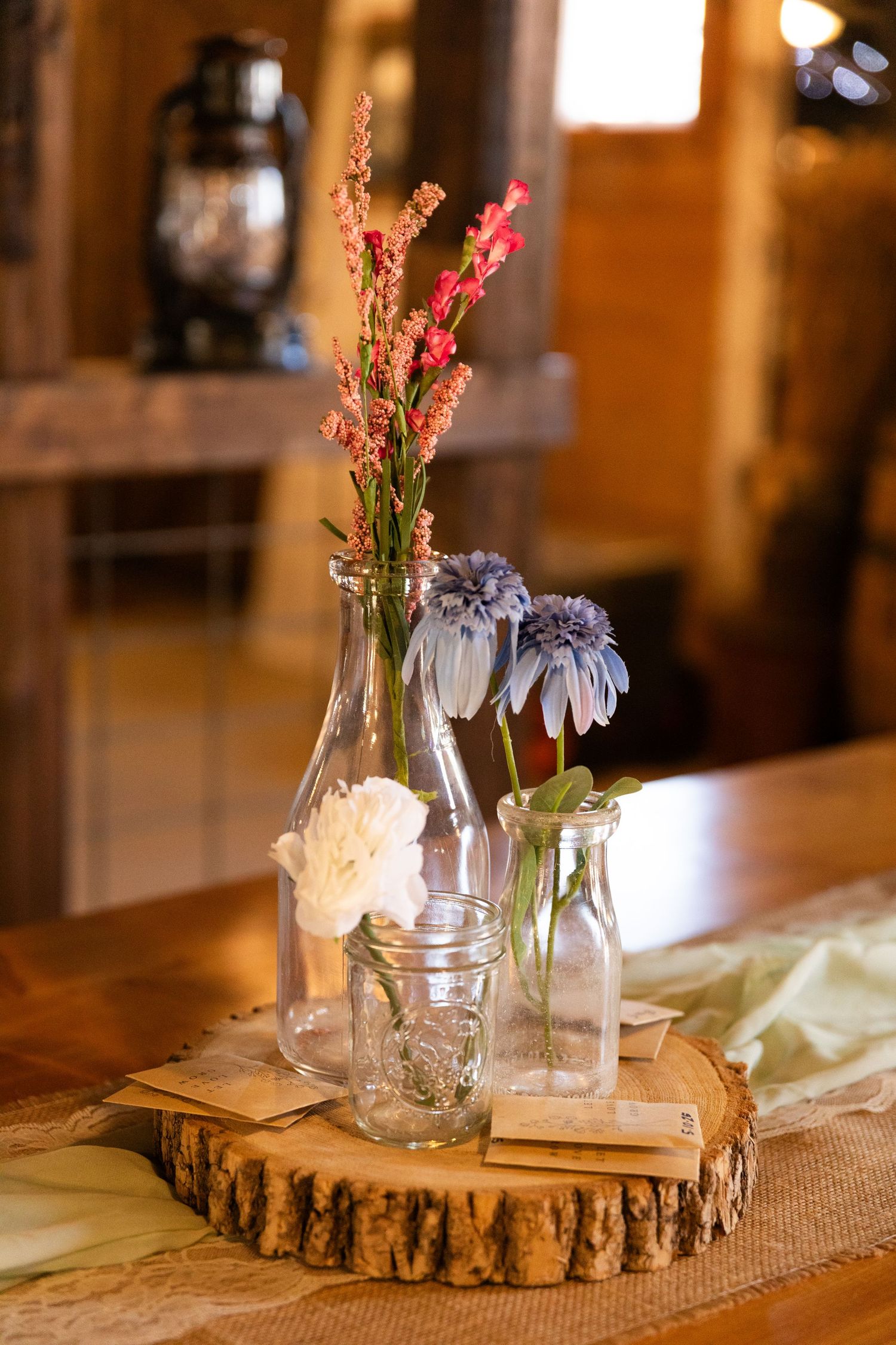 Rustic wedding centerpiece featuring glass bottles with flowers displayed on a wooden tree slice.