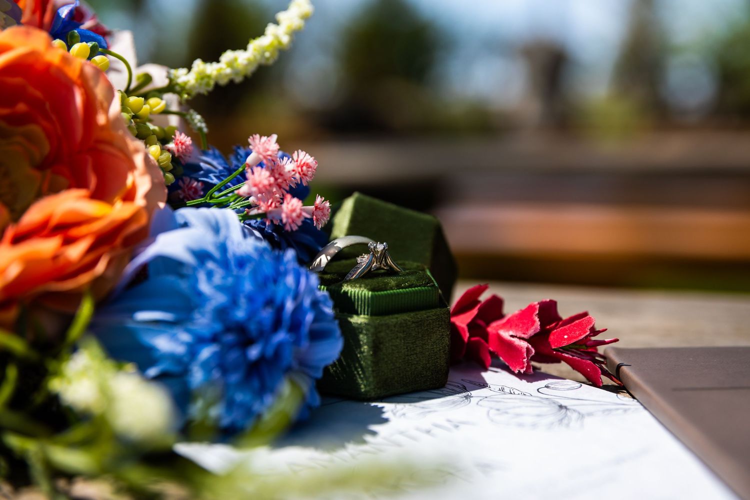Vibrant floral arrangements with blue, red and yellow blooms decorate a rustic outdoor wedding setting.