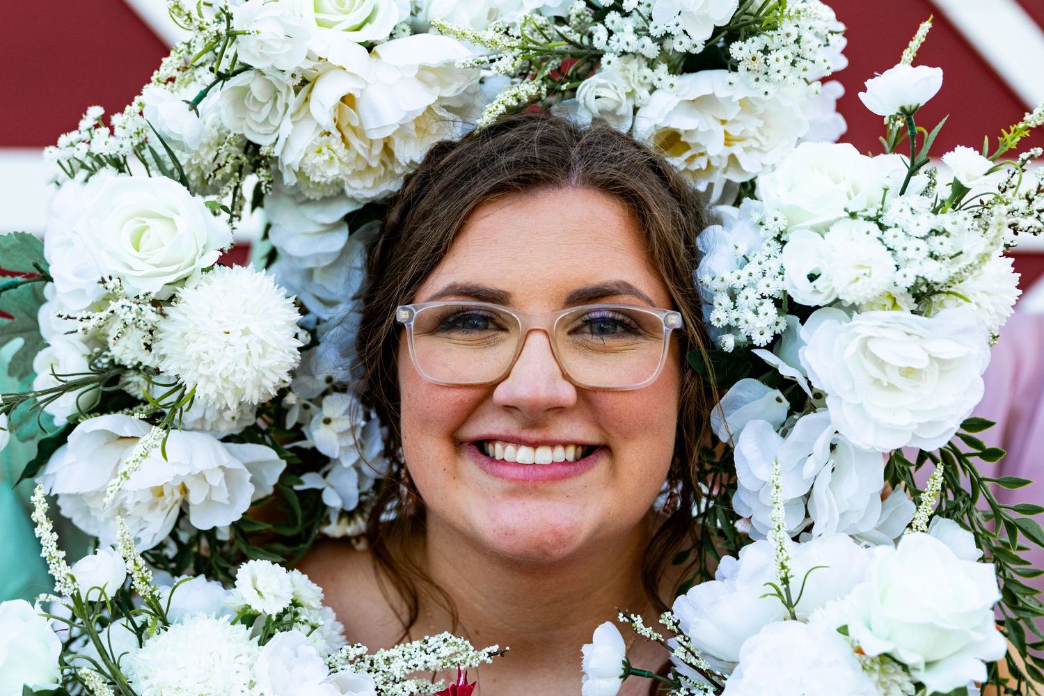 Wedding portrait framed by white flowers against red barn background.