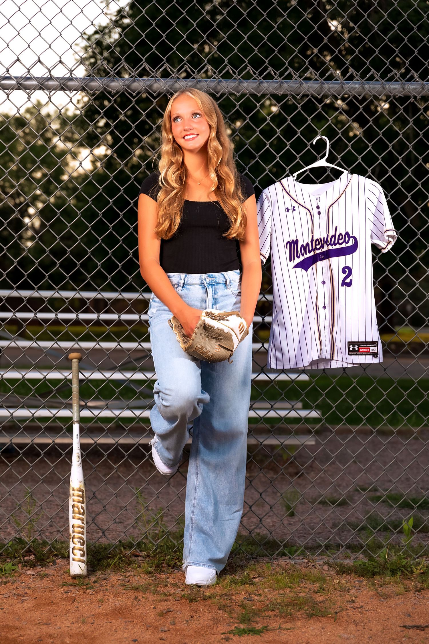 Baseball themed photo with jersey and glove against chain link fence backdrop.
