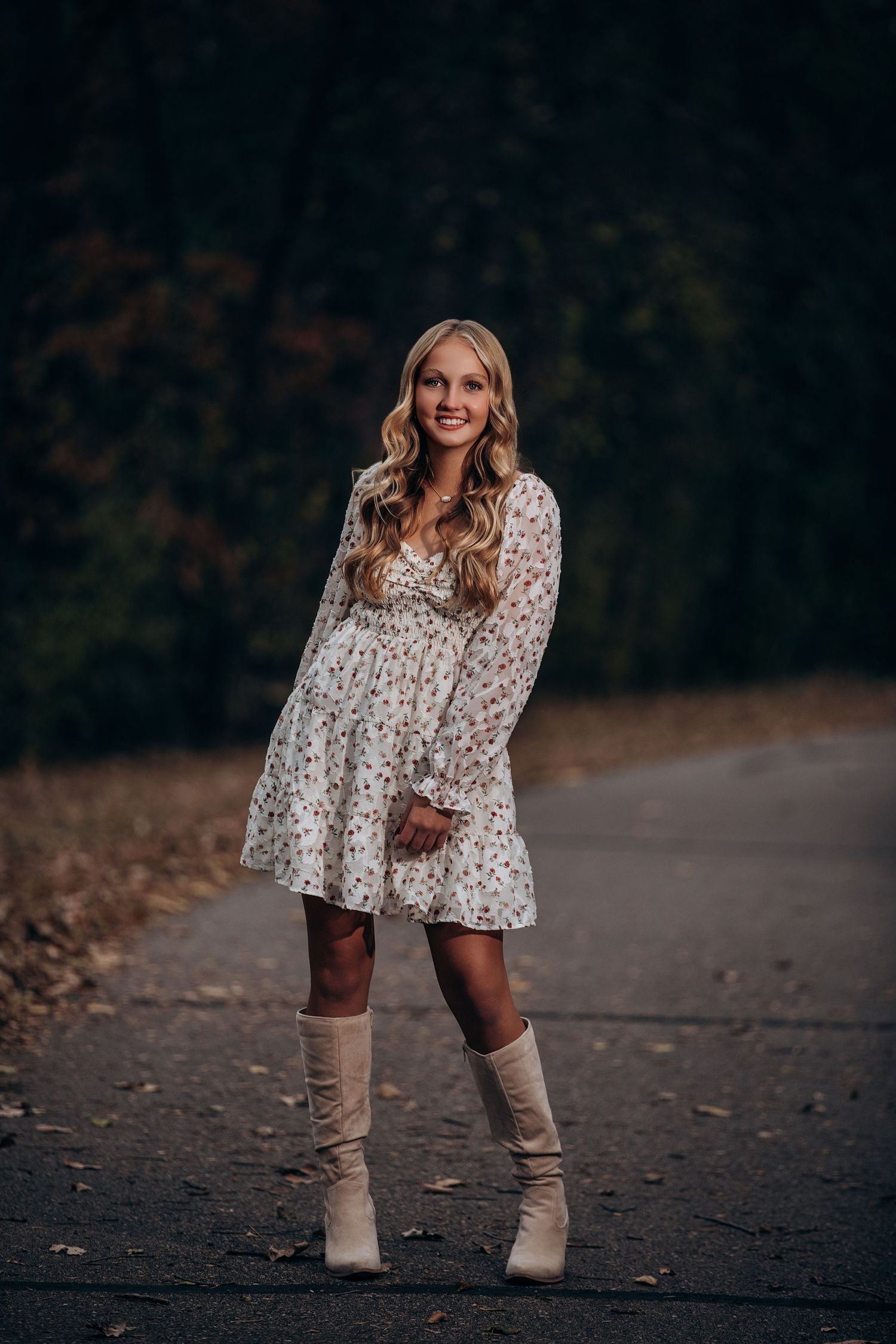 Fall fashion portrait with floral dress and tall boots on dark path.