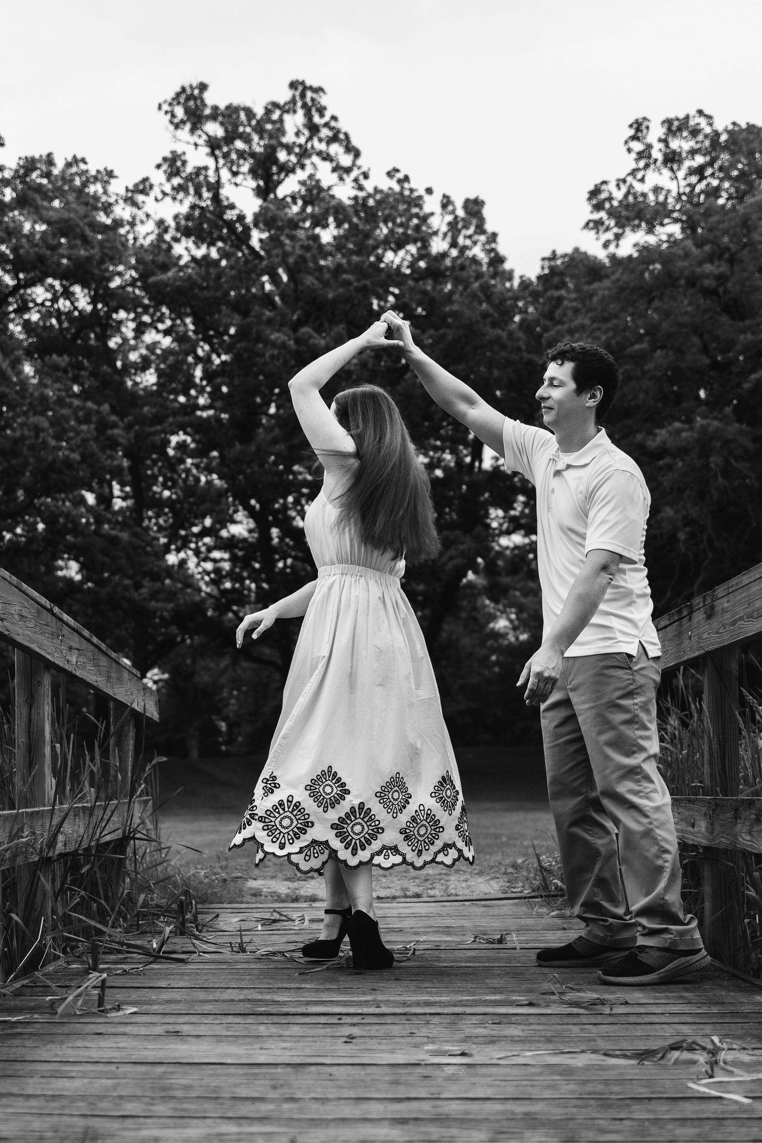 A couple dances romantically on a wooden bridge in black and white.