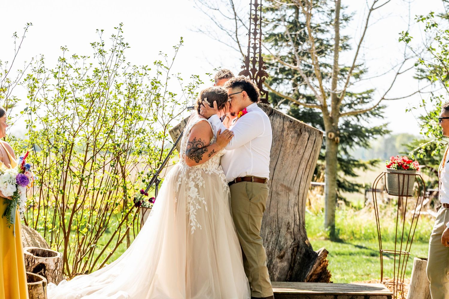Outdoor wedding ceremony taking place among trees and greenery in natural lighting.