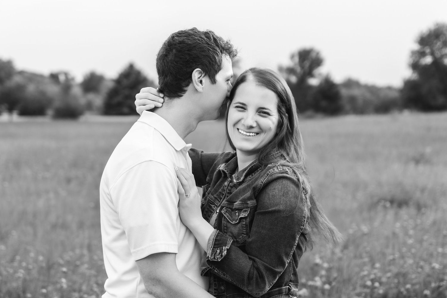 A happy couple shares romantic moments in a grassy field with wildflowers on a sunny afternoon.