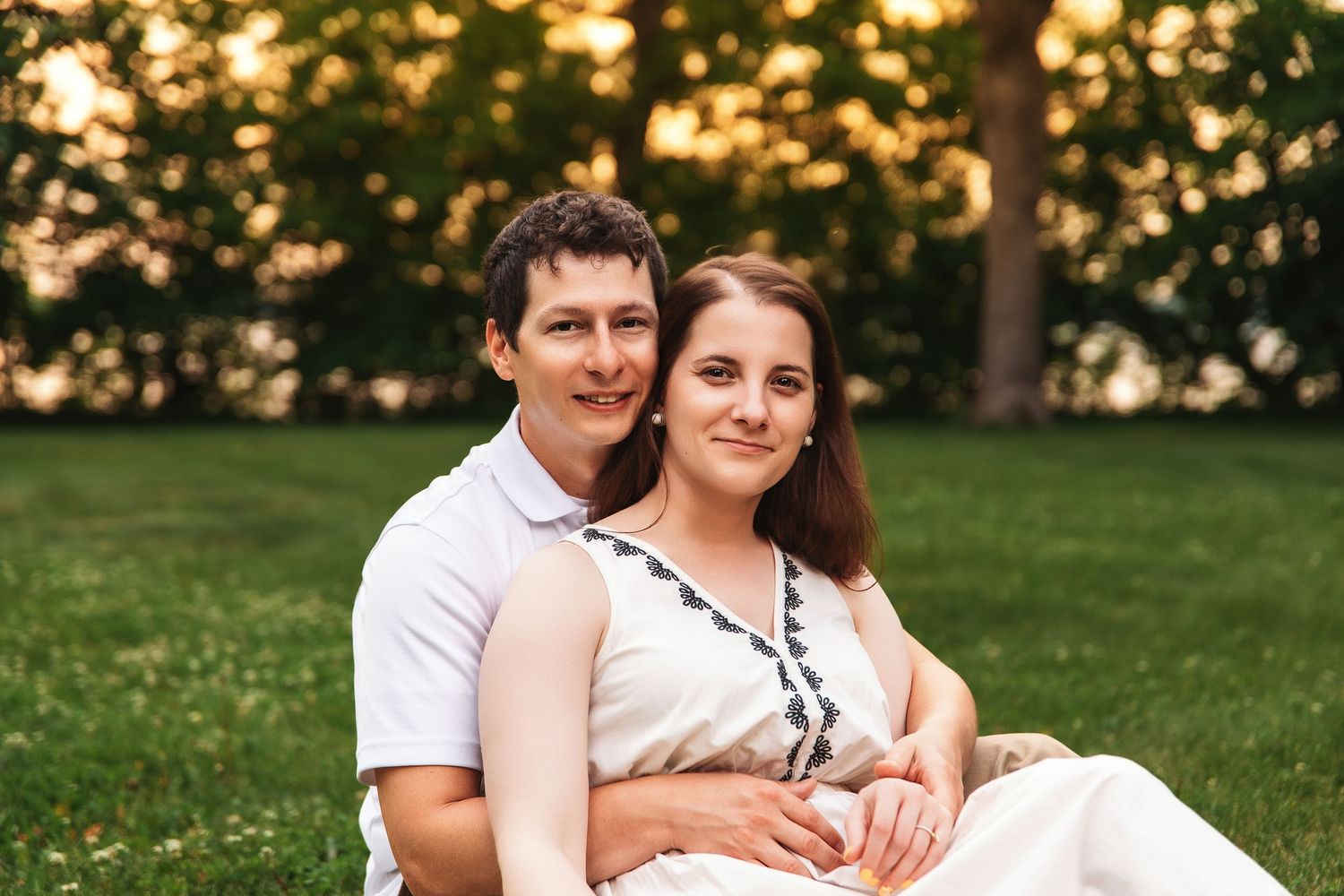 A couple relaxes together on grass during golden hour in a park setting.