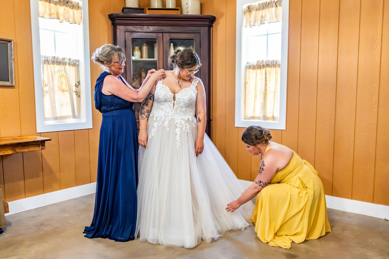 Wedding party members in blue and yellow dresses making adjustments to a white wedding gown.