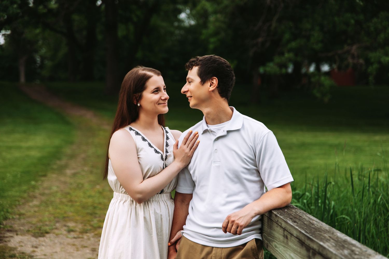 Romantic couple in white outfits walking and embracing along a lush green garden path in summer.