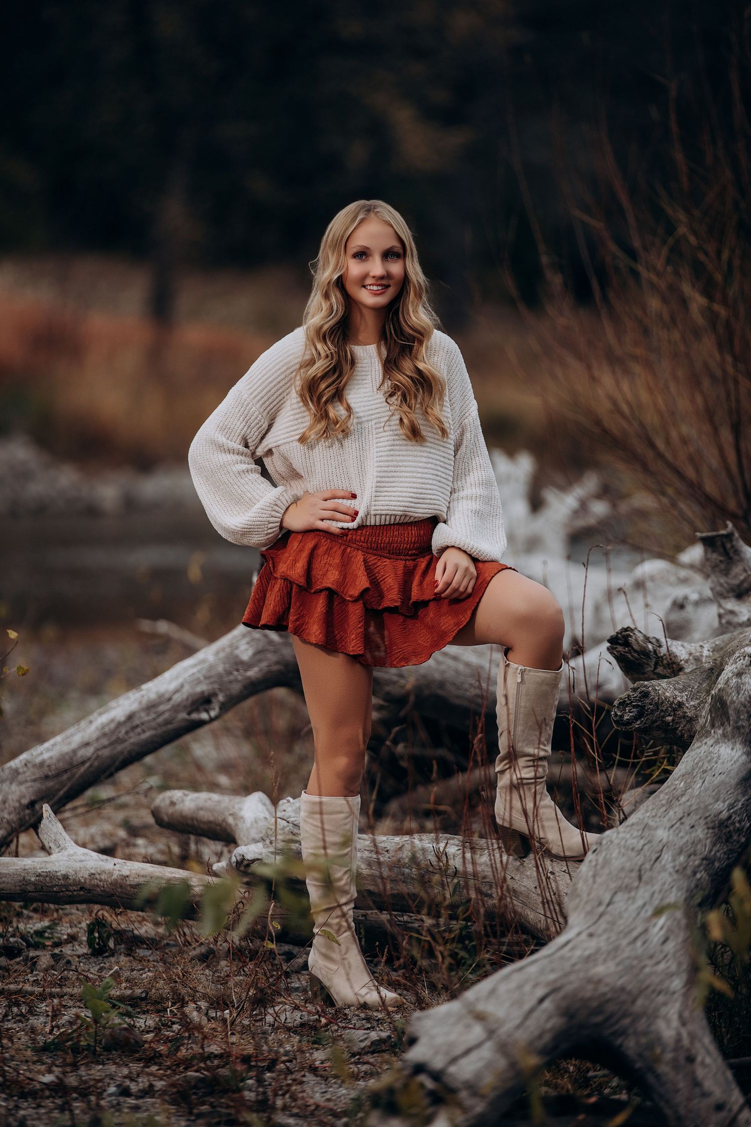 Rustic outdoor photo shoot with cream sweater and rust colored skirt among fallen logs.