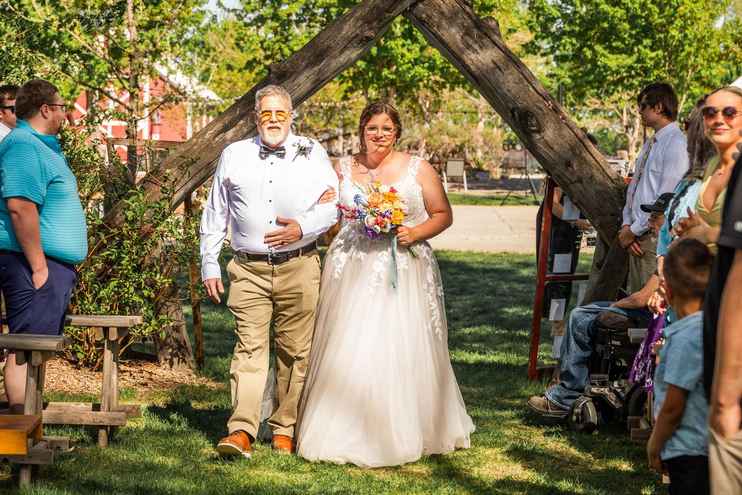 Wedding celebration outdoors under tree branches with guests gathered on a sunny day.
