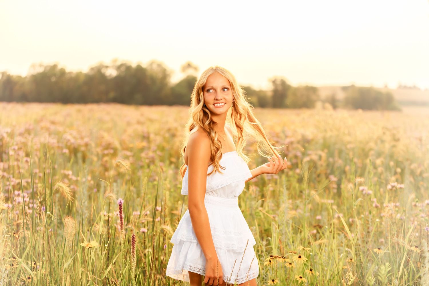 Woman in white sundress stands in golden field at sunset during summer portrait session.