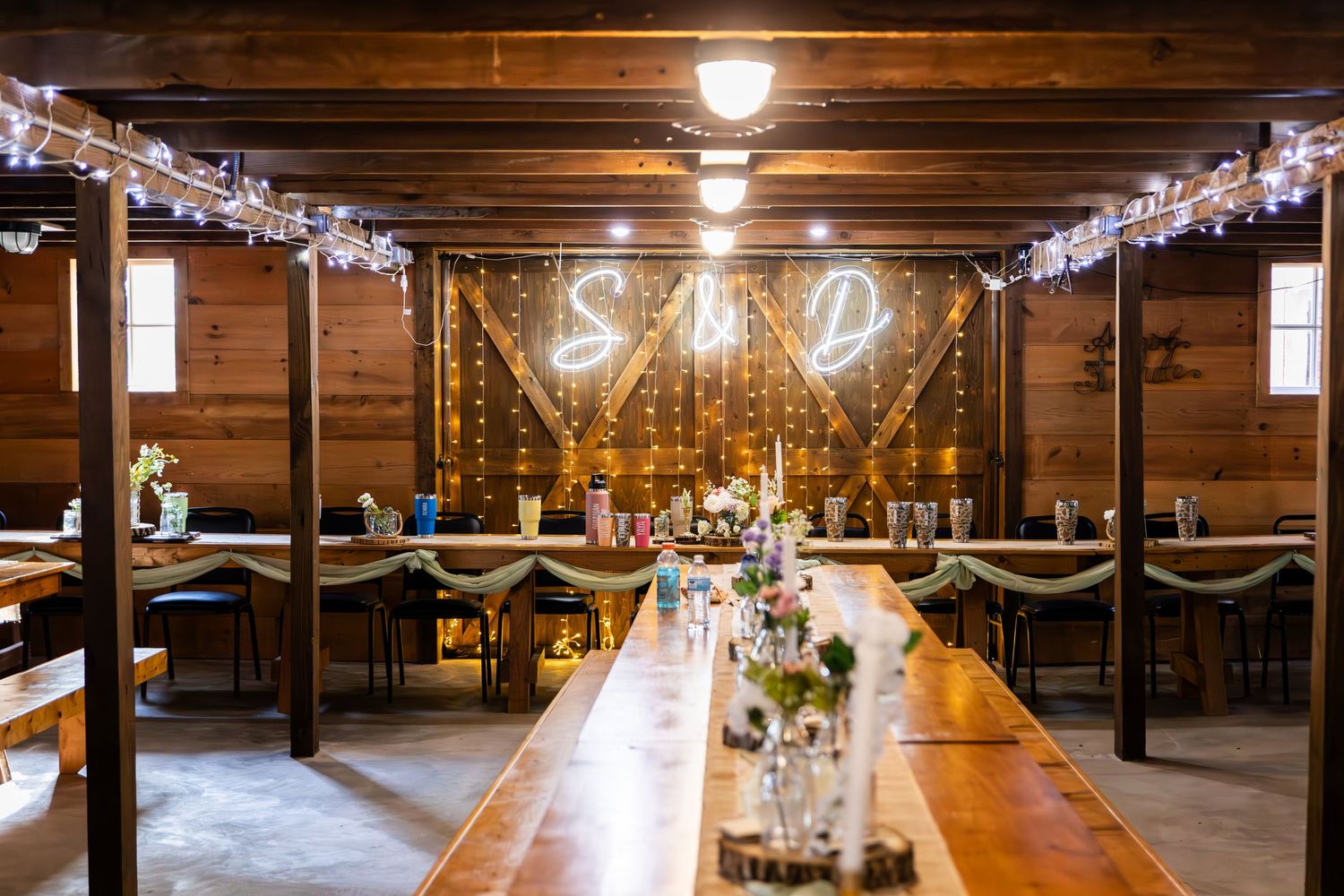 Rustic barn reception venue with exposed wooden beams and twinkling string lights creating ambient lighting.