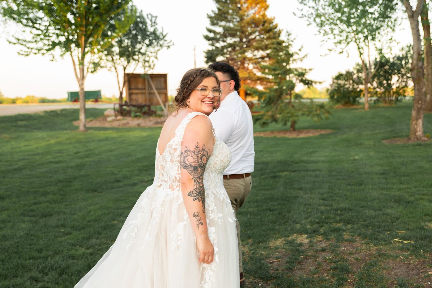 Couple celebrates their wedding day on lush green lawn with trees in background.