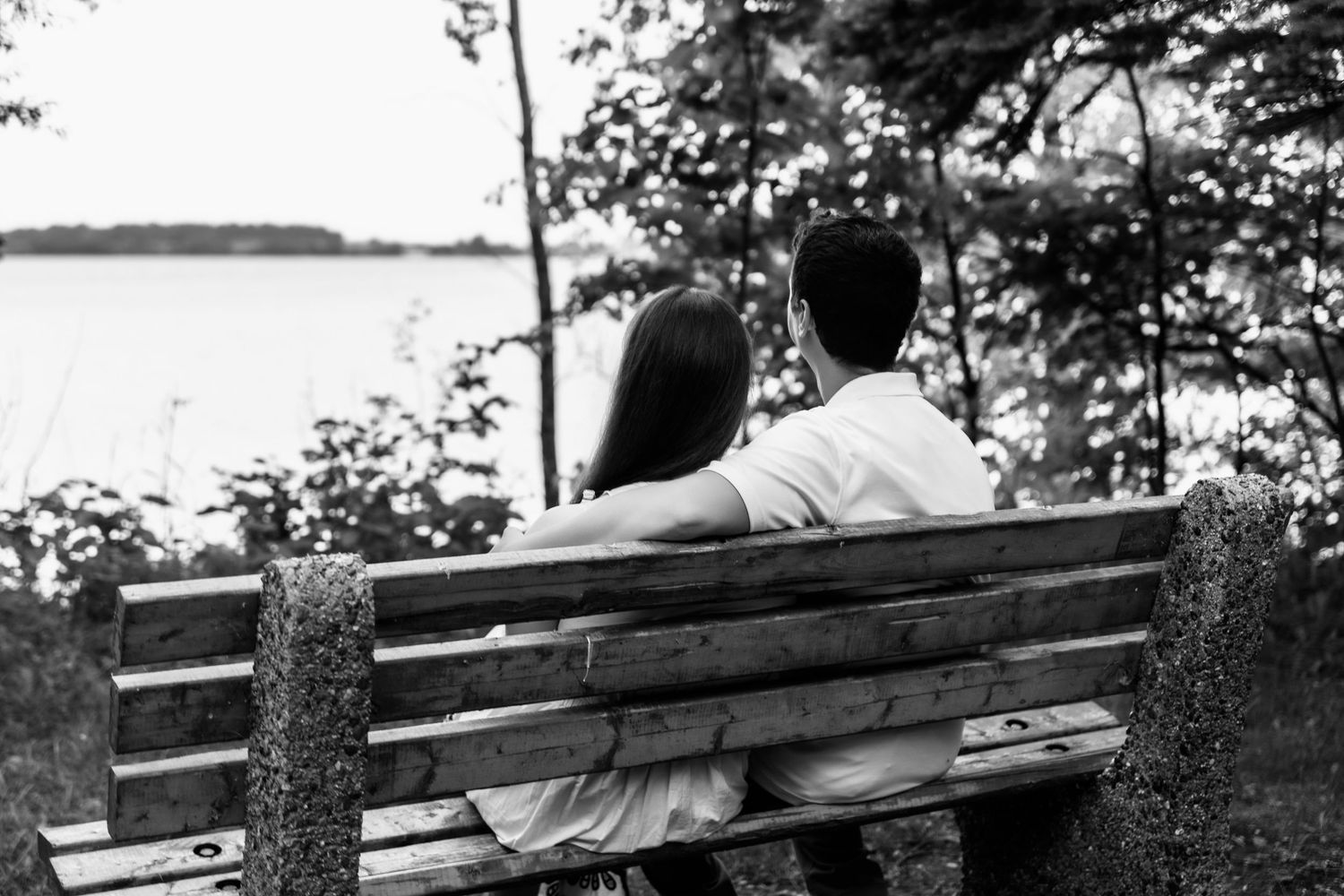 A couple sits together on a wooden bench overlooking a serene lake view.