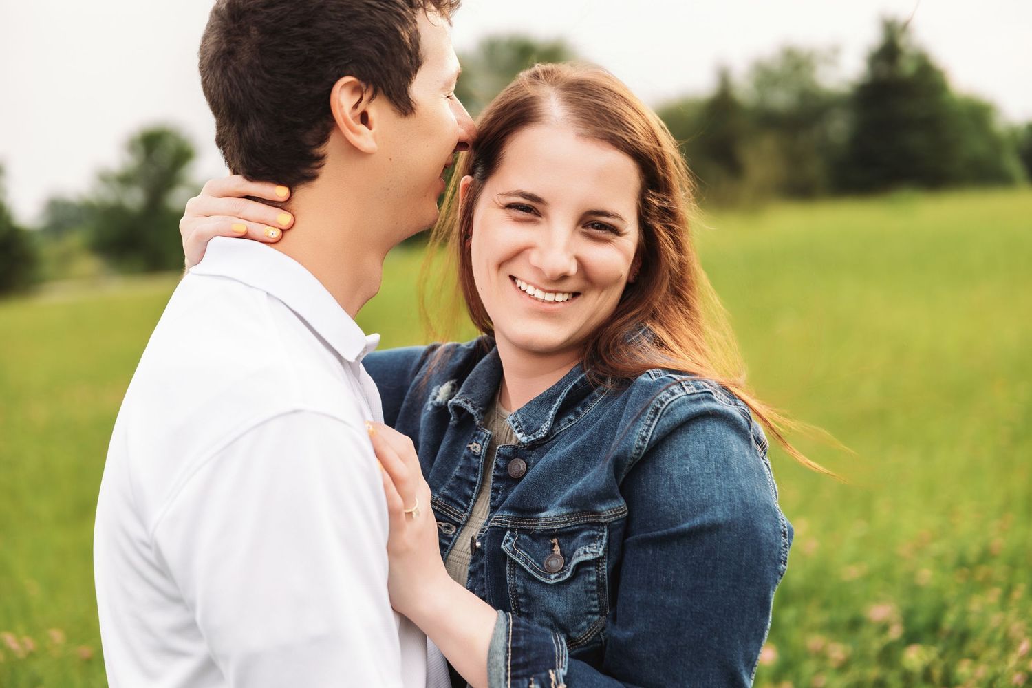 A happy couple embraces in a sunny meadow while wearing white and denim clothing.