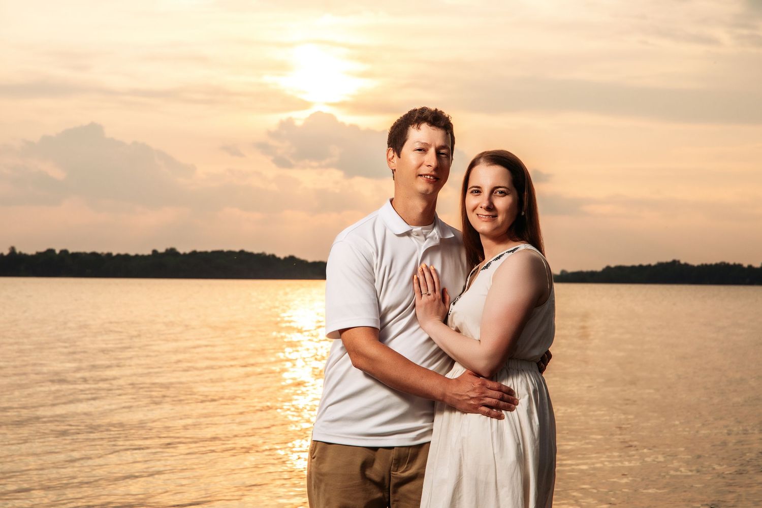 A couple embraces against a golden sunset over water in summer evening light.