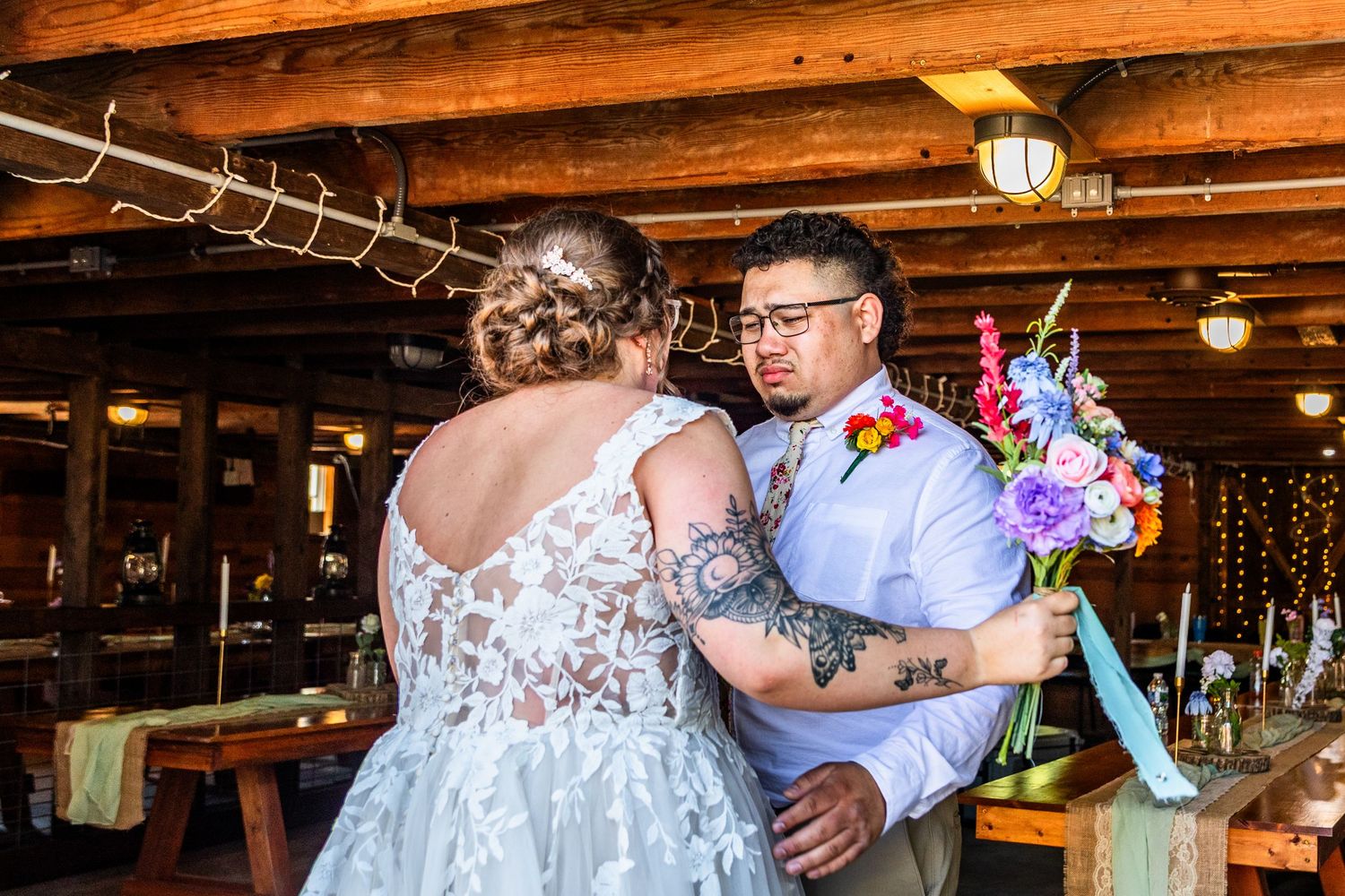 Newlywed couple dancing together at rustic barn wedding reception venue with exposed wooden beams and romantic lighting.