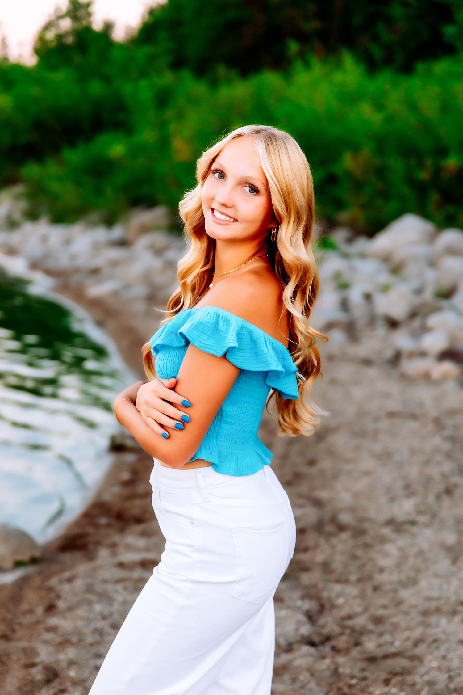 Summer portrait by waterfront wearing blue off-shoulder top and white pants.