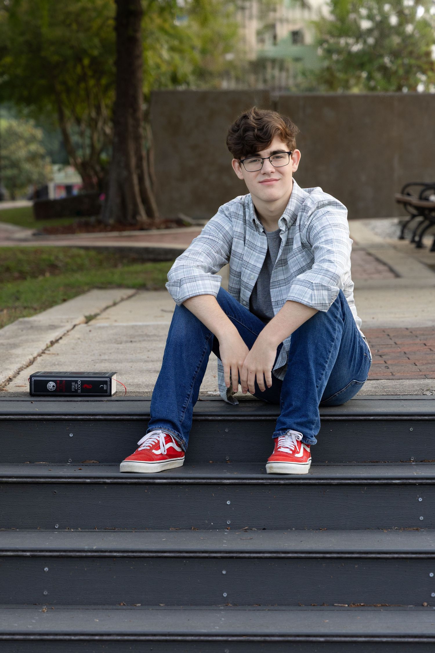 Class of 2025 senior portrait, relaxed pose on river steps with favorite history book at Milton Riverwalk, Santa Rosa County, FL.