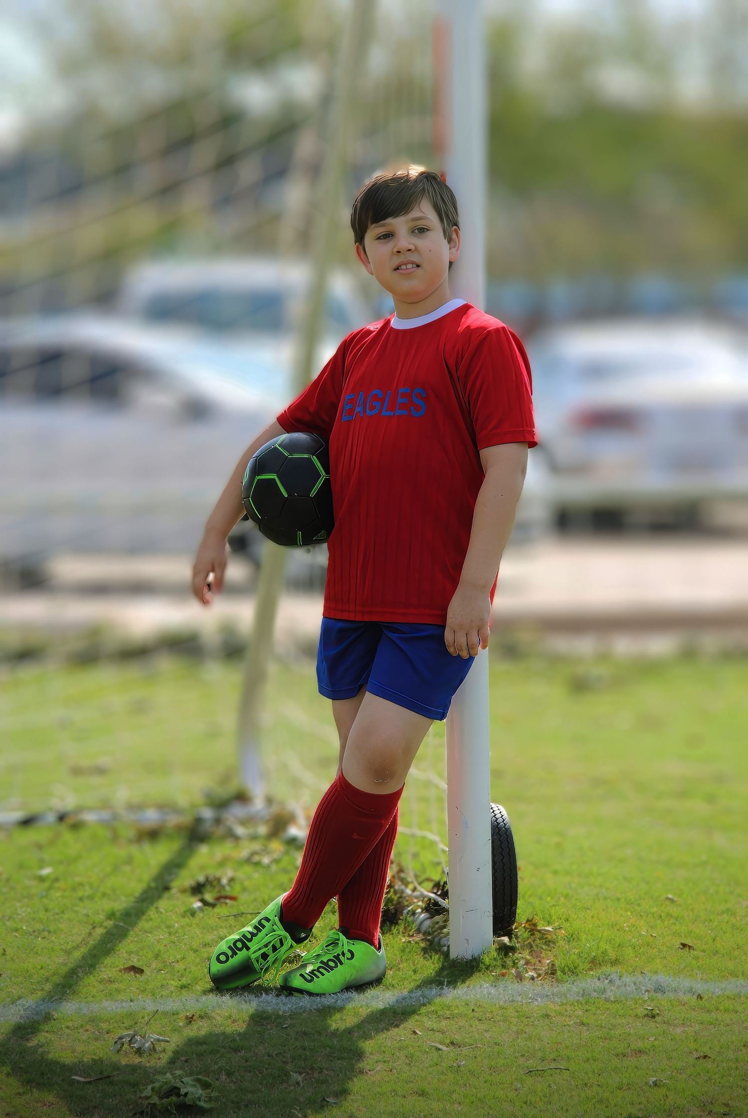 Full-color natural light portrait of 4th grade soccer boy leaning on goalpost with ball—relaxed and confident. Photography by Rachel.