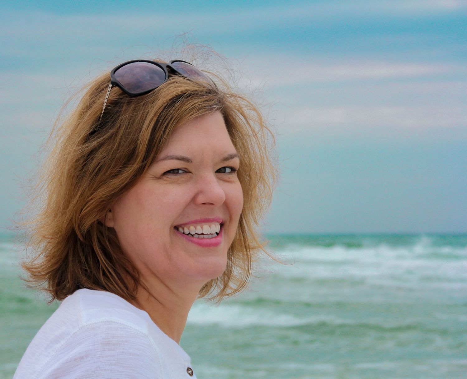 Candid beach portrait of a smiling woman in her 40s at Navarre, FL—gorgeous colors, soft light, and natural beauty. Photography by Rachel.