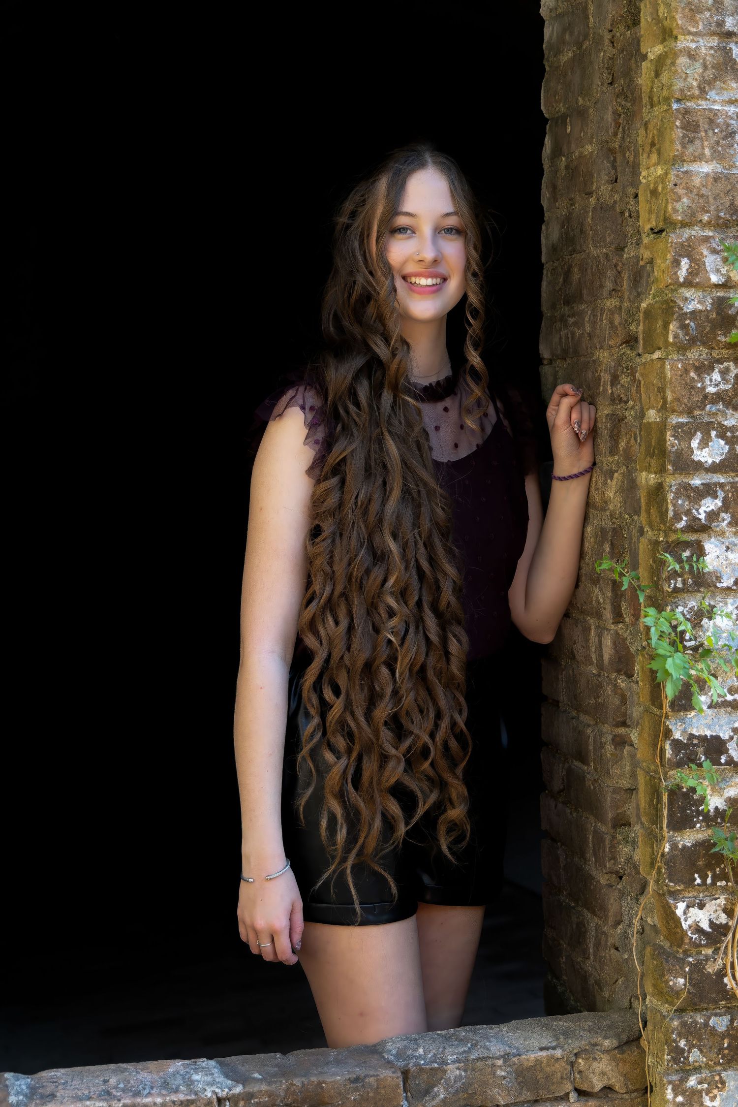 Senior portrait of a girl at Fort Pickens, FL—full length in black shorts & burgundy top, framed by brick wall. Photography by Rachel.