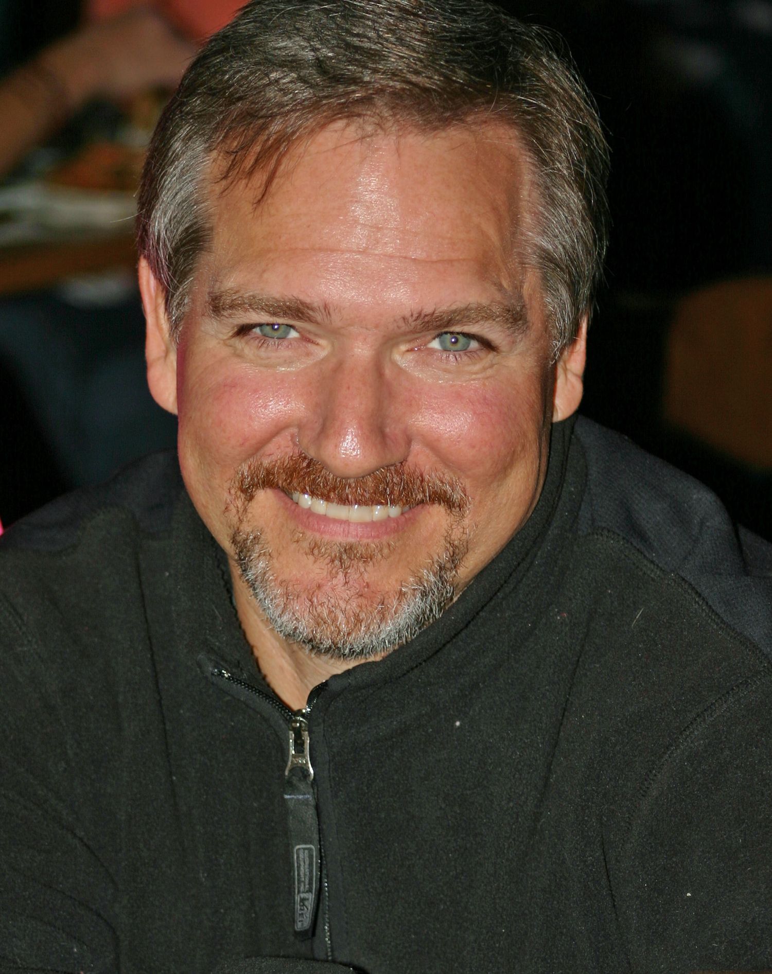 Candid close-up portrait of handsome man with blue eyes in Pensacola, FL—warm smile, casual fleece jacket. Photography by Rachel.