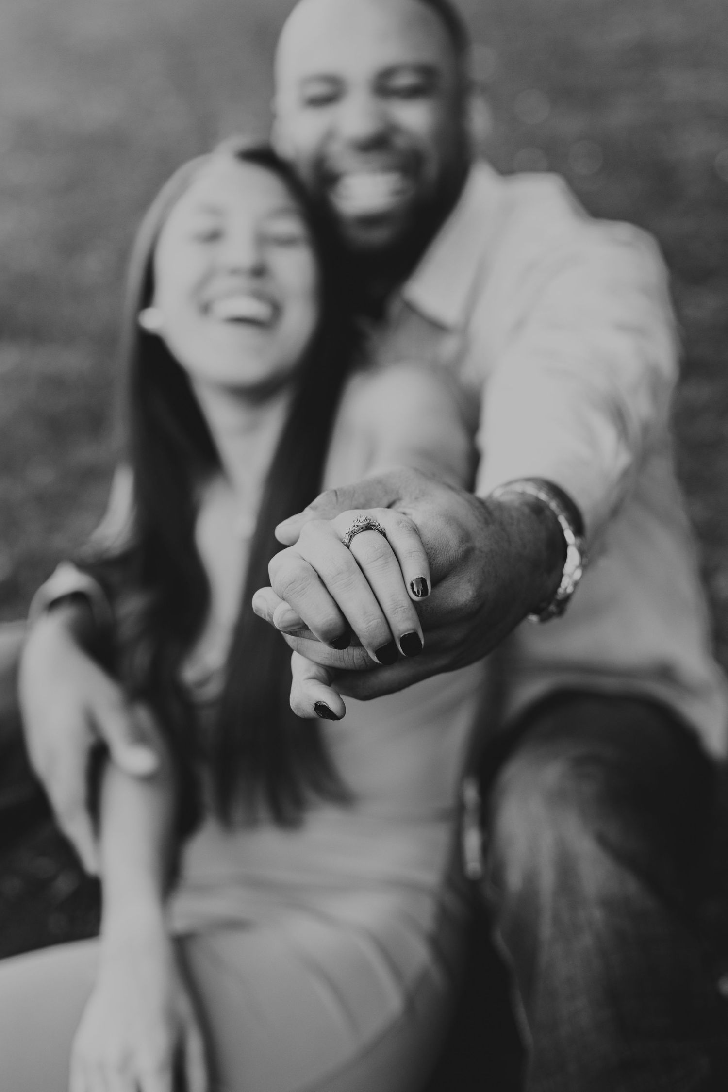 A black and white engagement photo showing hands with rings in focus.