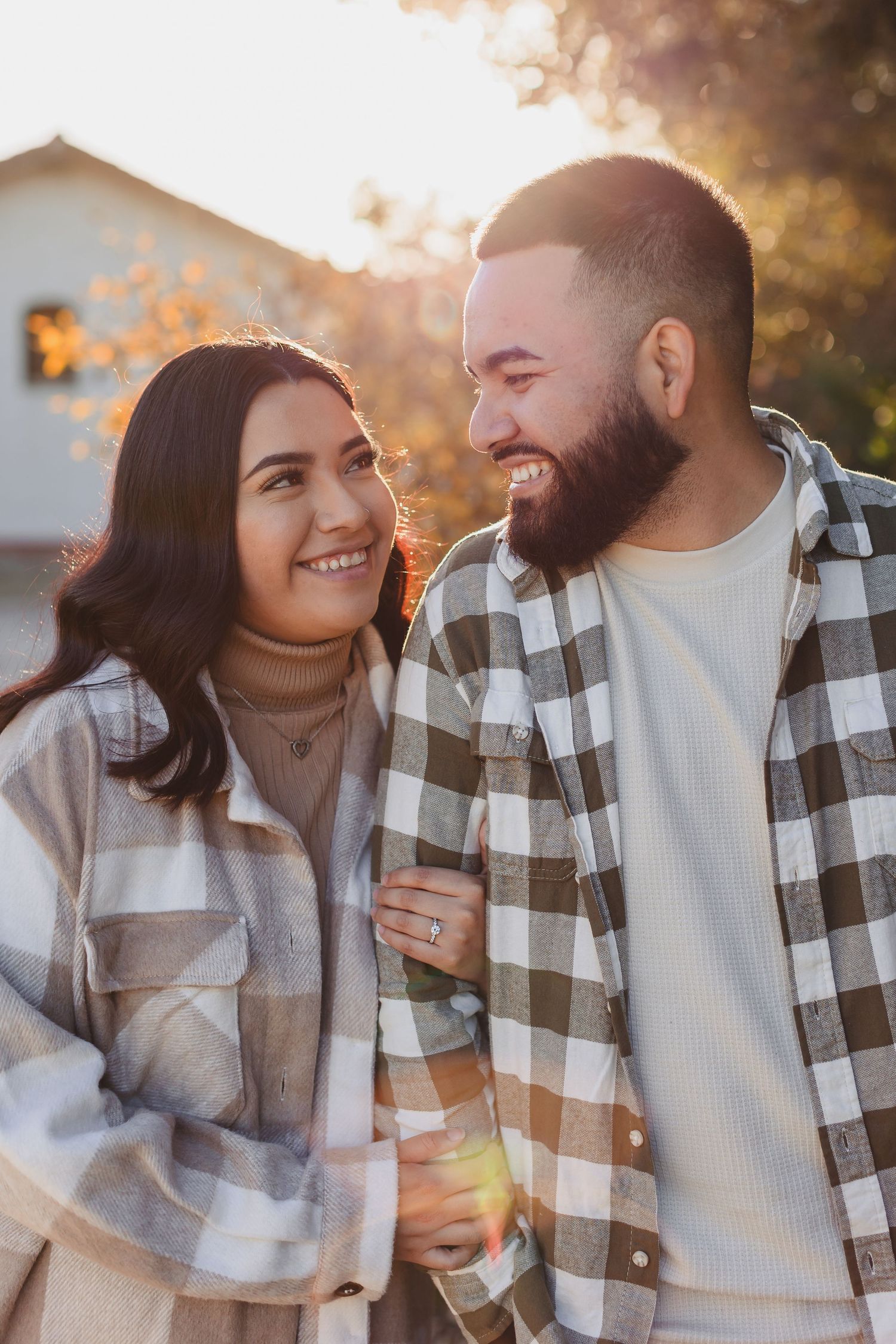 Couple in matching plaid jackets smiling at each other in warm sunset light.