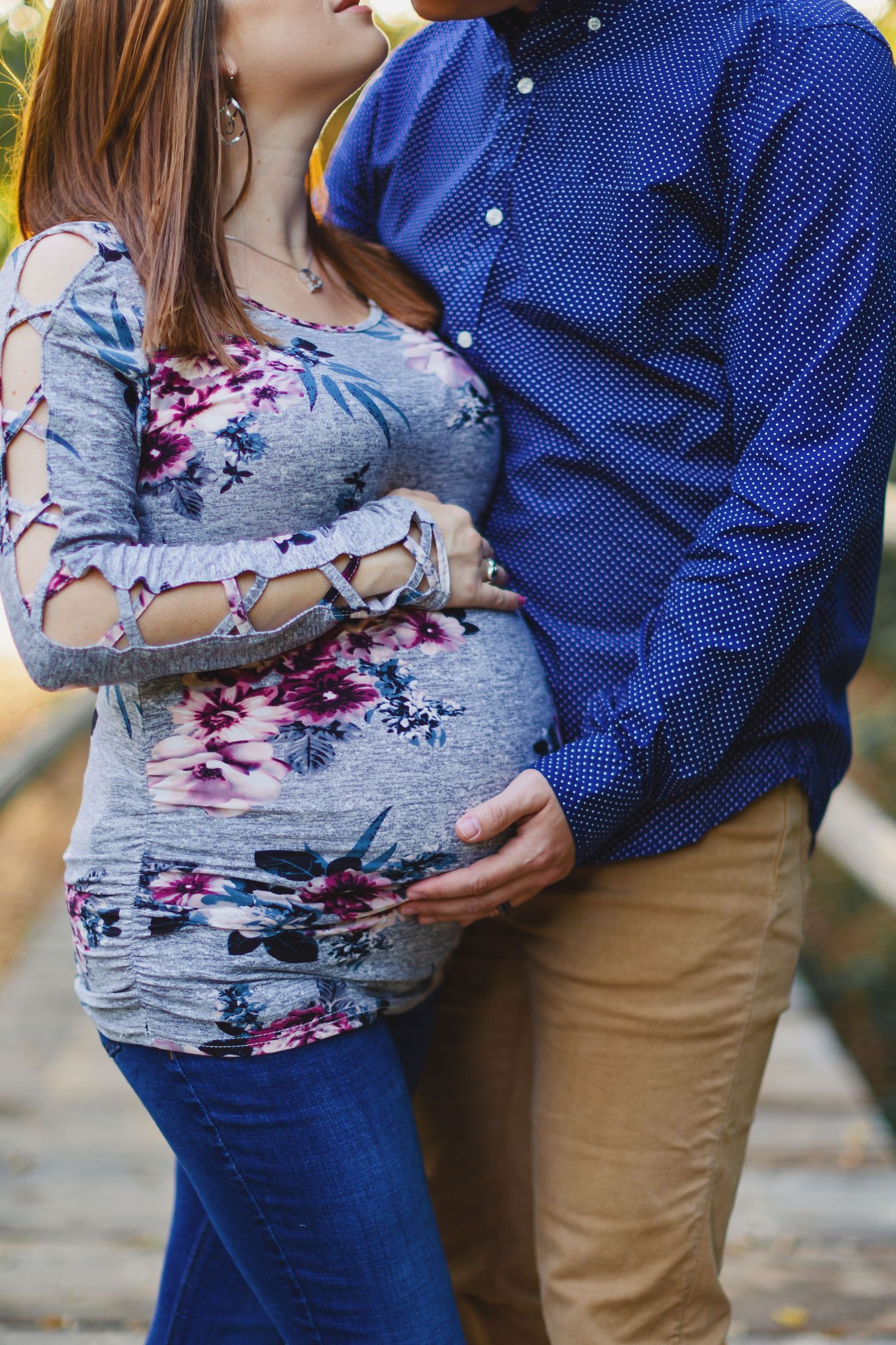 Close-up of couple's embrace highlighting floral maternity top and baby bump.