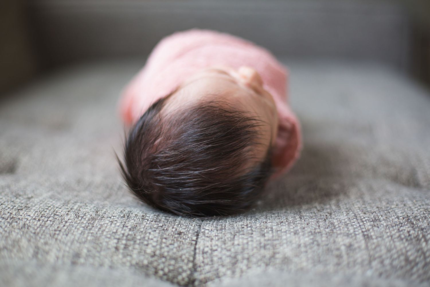 Dark-haired infant resting peacefully on gray textured surface.