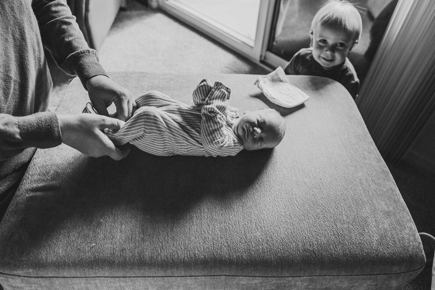 Black and white photo of a baby being changed on a changing table with family member helping.