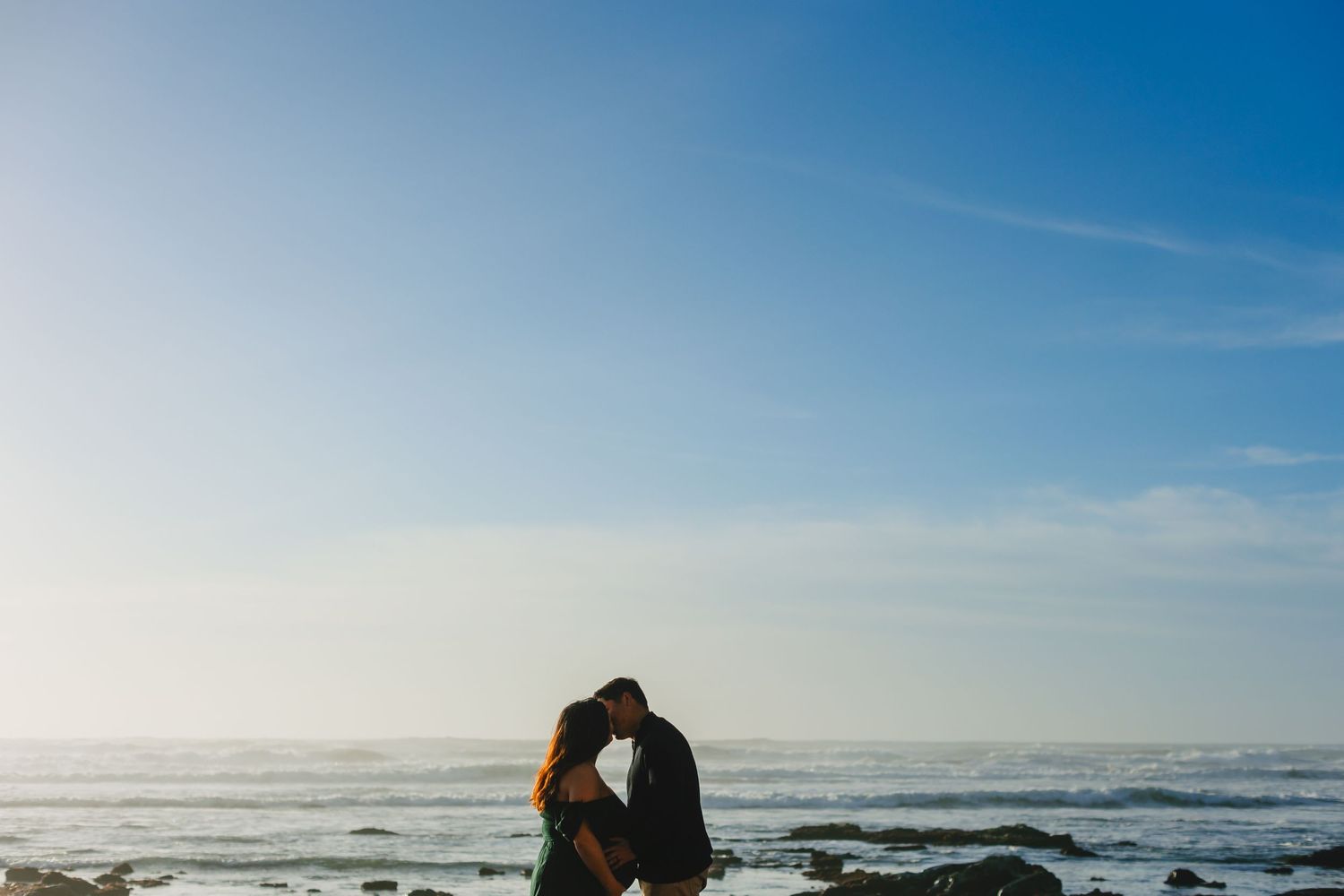 Silhouetted couple embraces against ocean horizon during sunset.