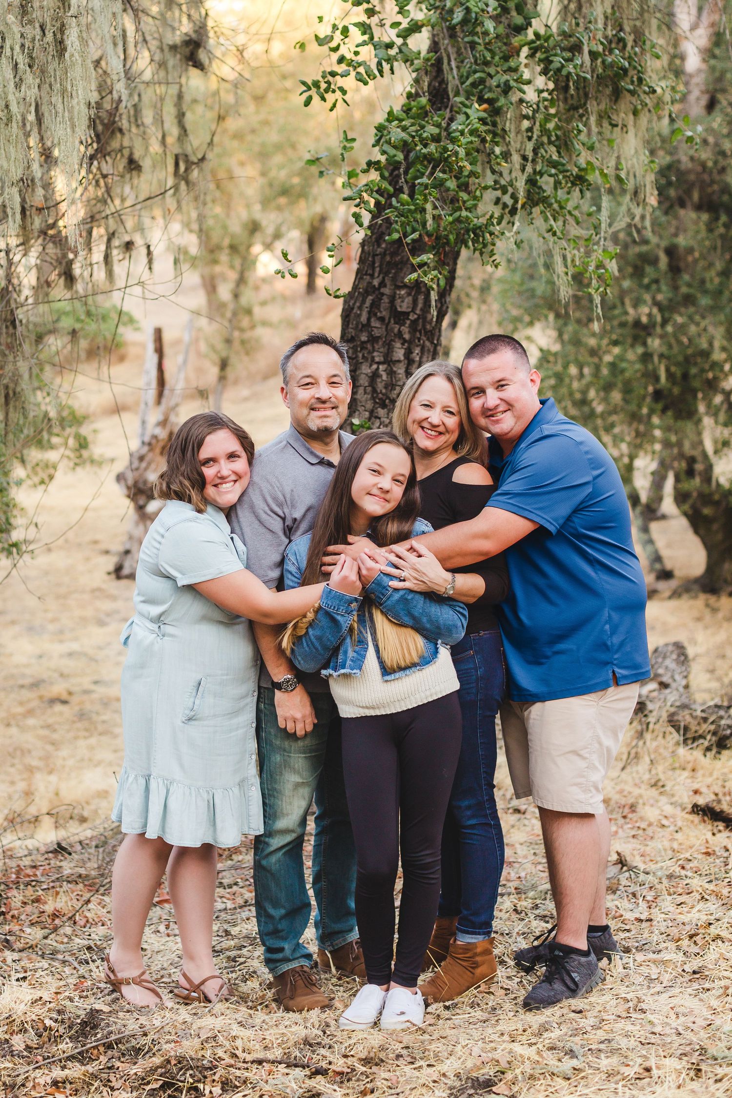 A cheerful group embraces in a tight hug while standing among trees at sunset.