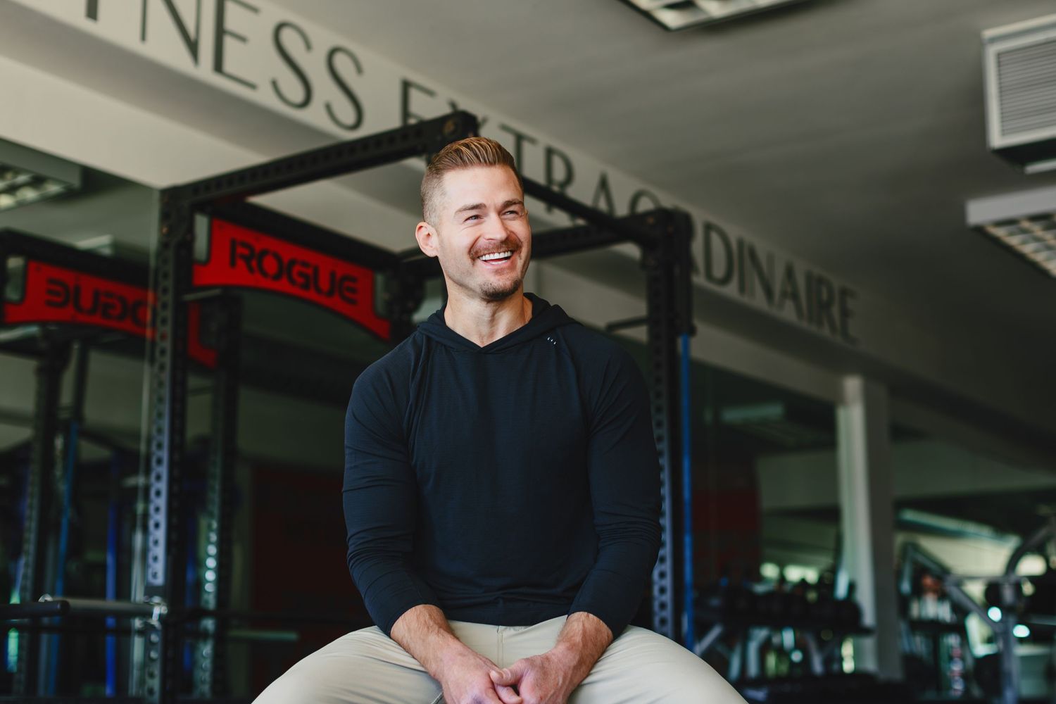 A person in a dark sweater smiling while sitting in a fitness center.
