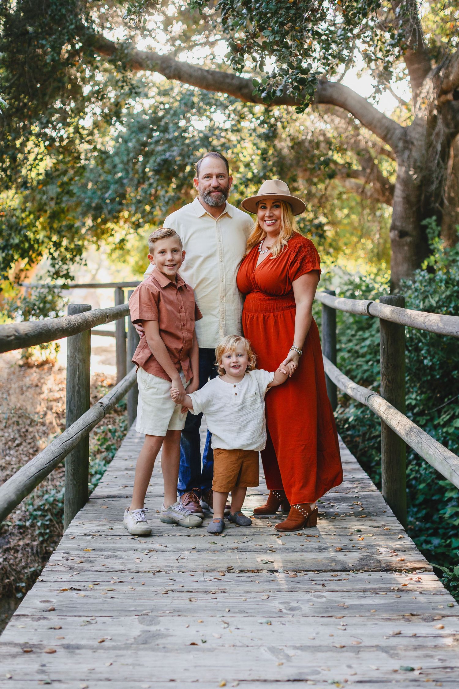 Family of four poses together on a wooden bridge surrounded by lush greenery.