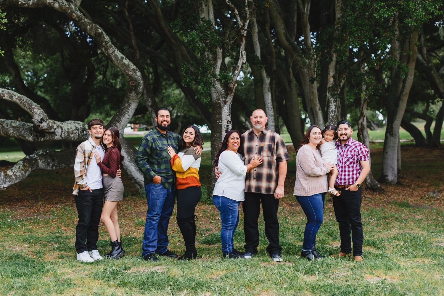 Group of friends enjoying an outdoor gathering under large trees in a park setting.