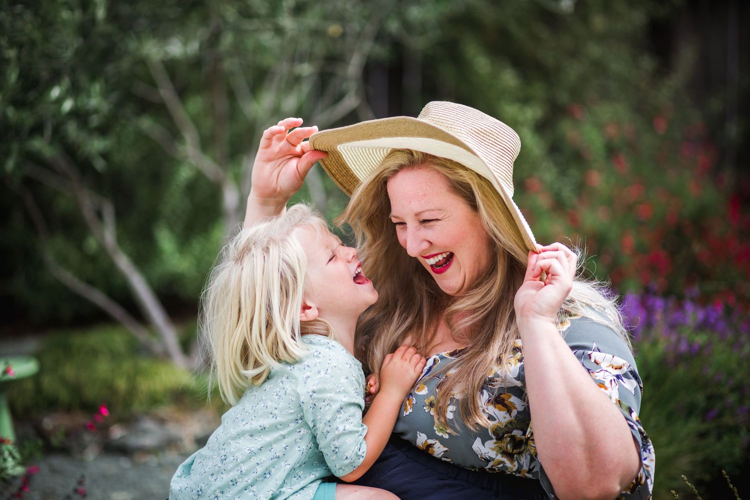 Two people sharing a playful laugh in a garden while wearing summer attire.