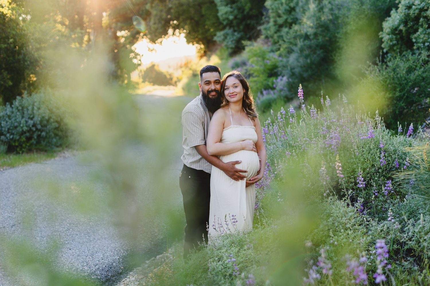 Couple embraces during maternity photoshoot in blooming garden at sunset.