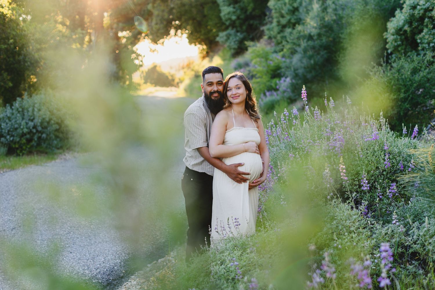 A couple embraces in a garden at sunset with purple wildflowers blooming along a serene pathway.