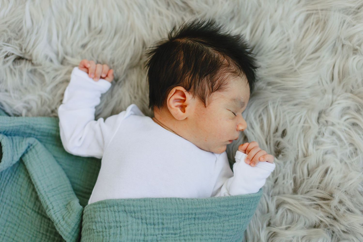 Sleeping infant in white onesie on fluffy blanket with teal cover.