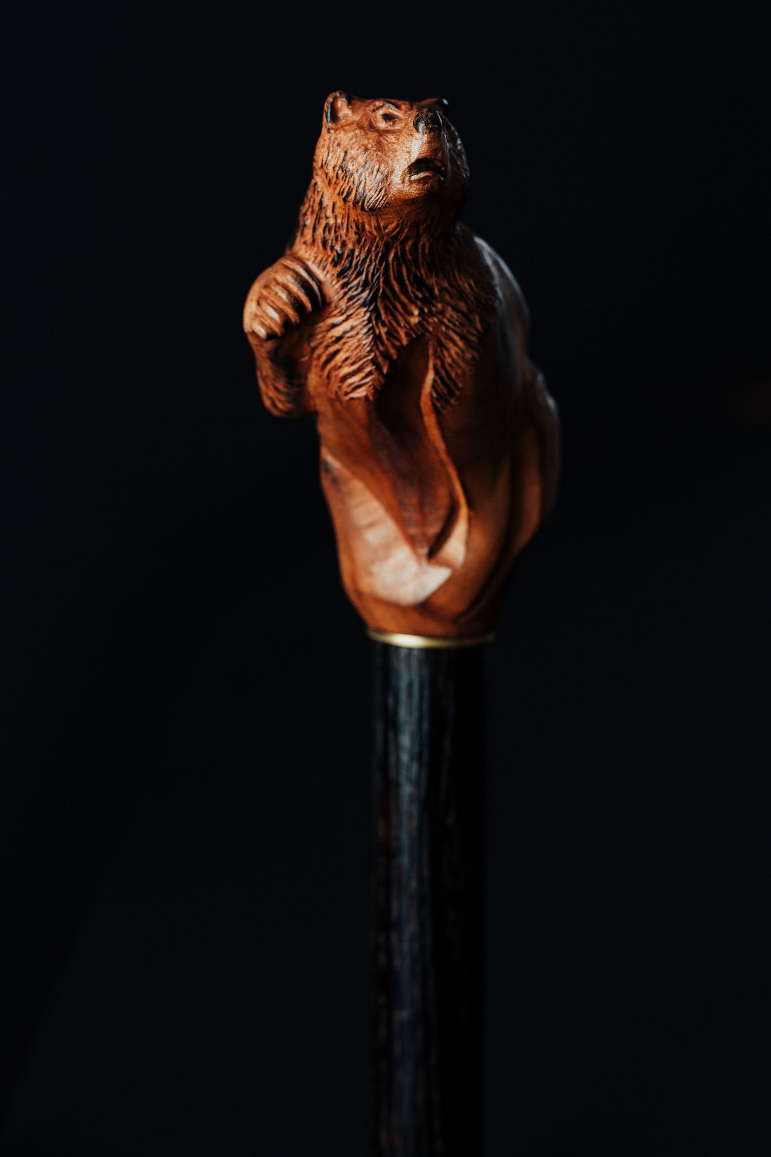 Decorative wooden bear carving mounted as a walking stick handle against black background.
