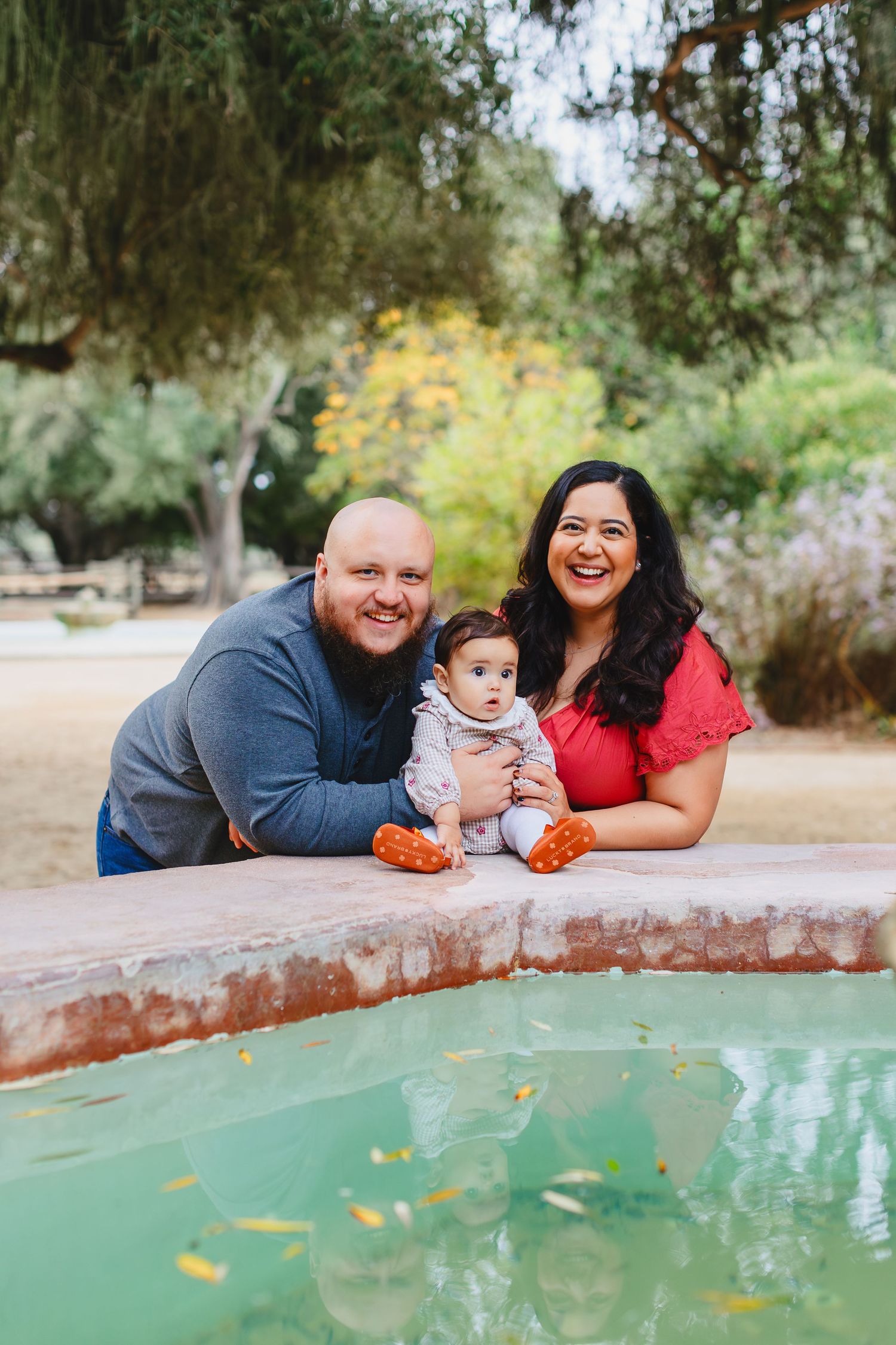 A happy family poses together by a pool with their baby on a sunny day in a garden setting.
