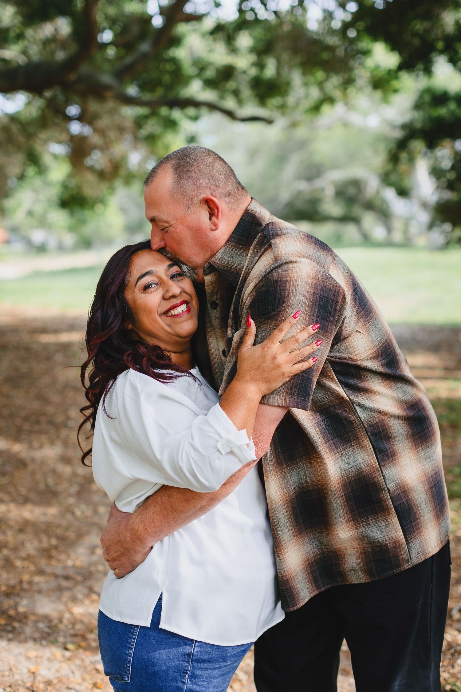 A couple sharing a joyful embrace outdoors under trees with genuine laughter and affection.