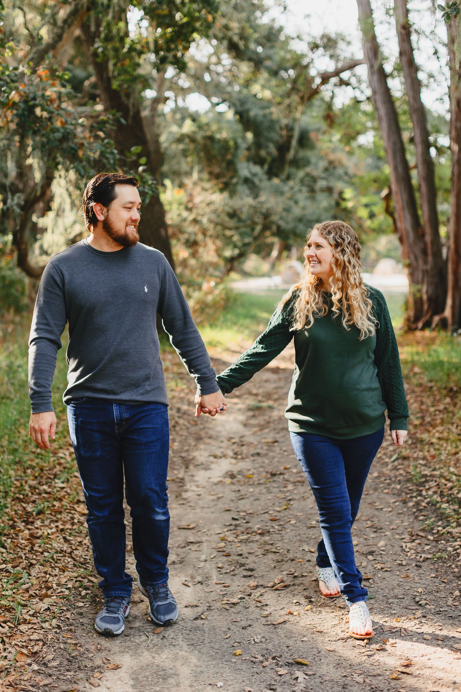 Couple walking hand in hand on nature trail surrounded by autumn trees.