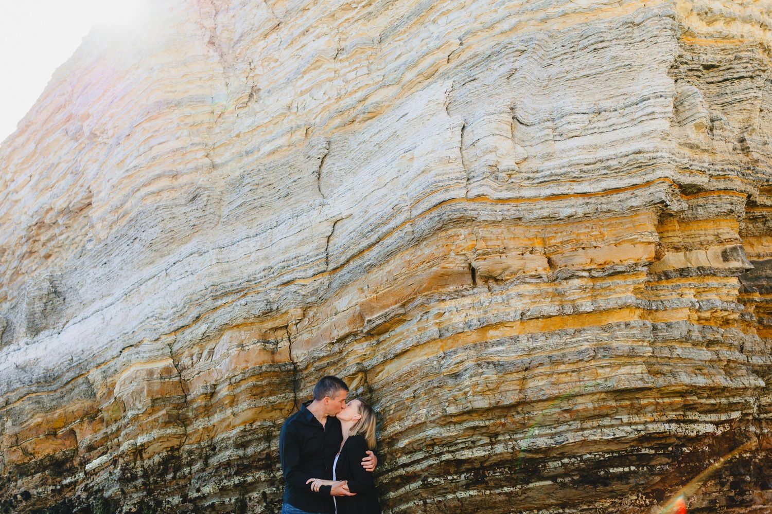 Intimate couple moment against dramatic layered rock cliff formations.