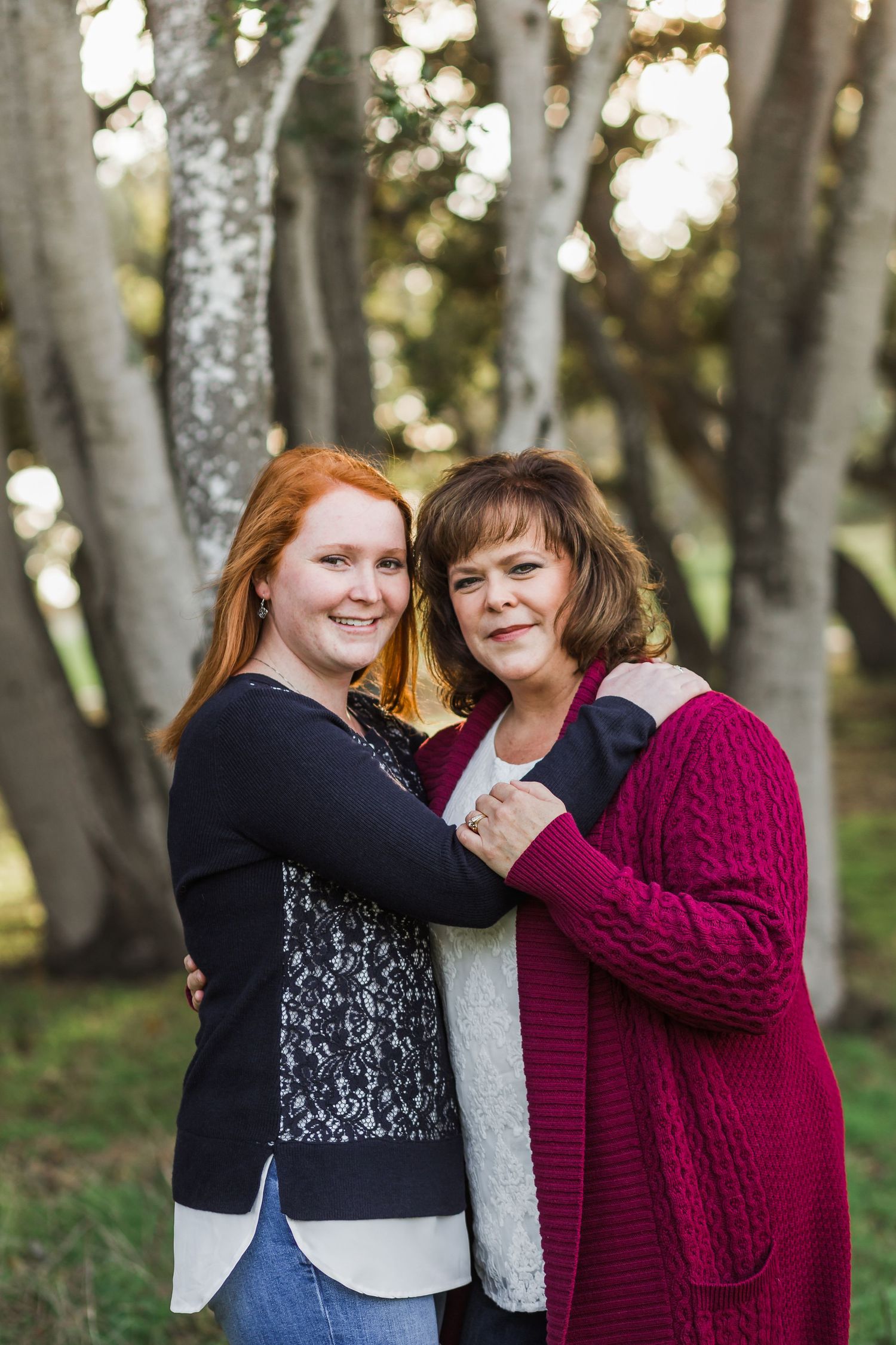 Two people embracing while standing among trees in casual winter attire.