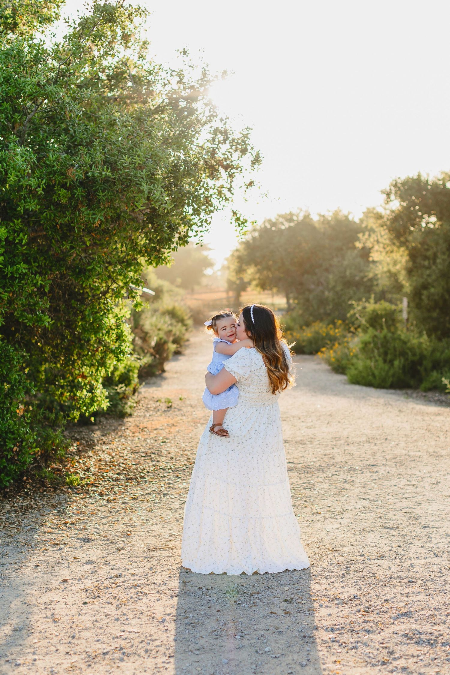 A tender moment between parent and child on a sunlit dirt path surrounded by greenery.