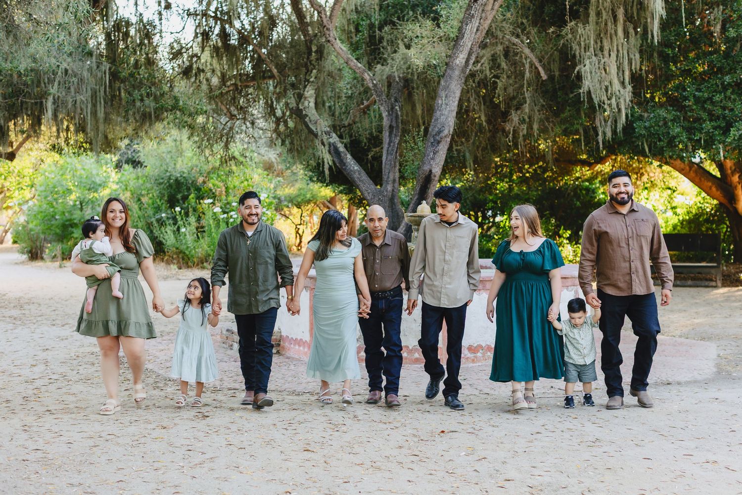Multi-generational group walks together on a sandy path surrounded by lush greenery and Spanish moss.