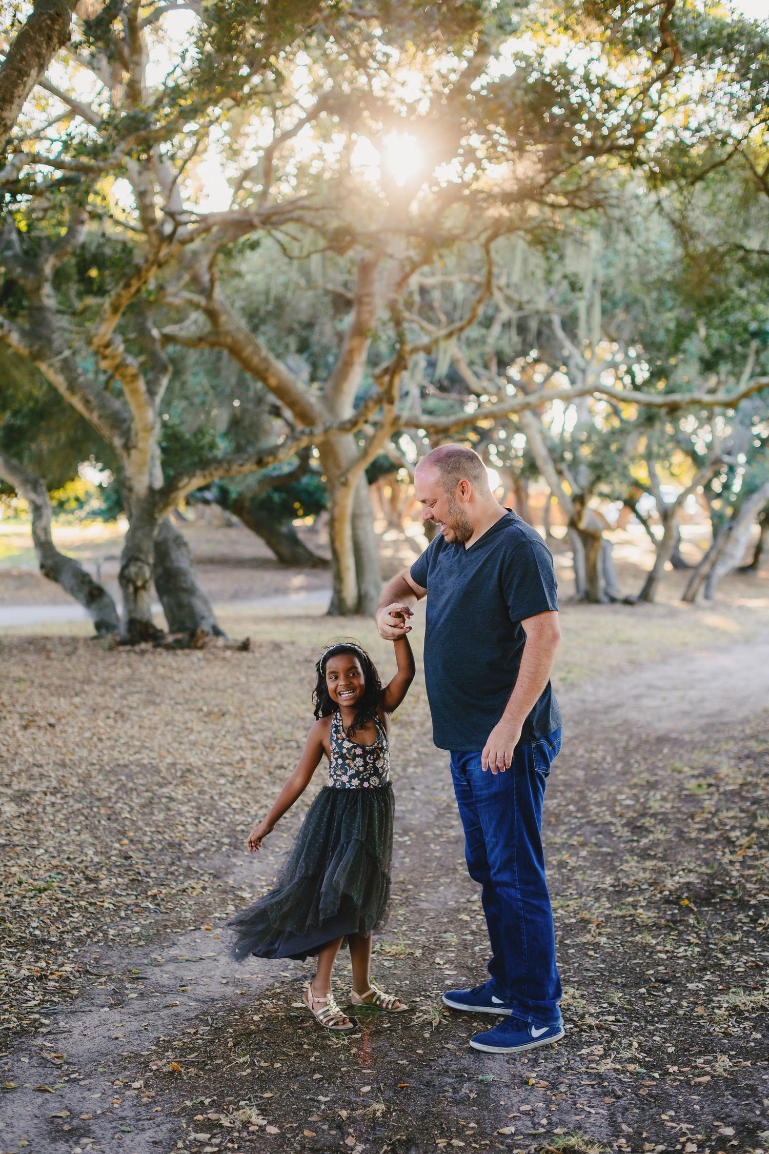 Adult and child share a joyful moment dancing together under sunlit trees.
